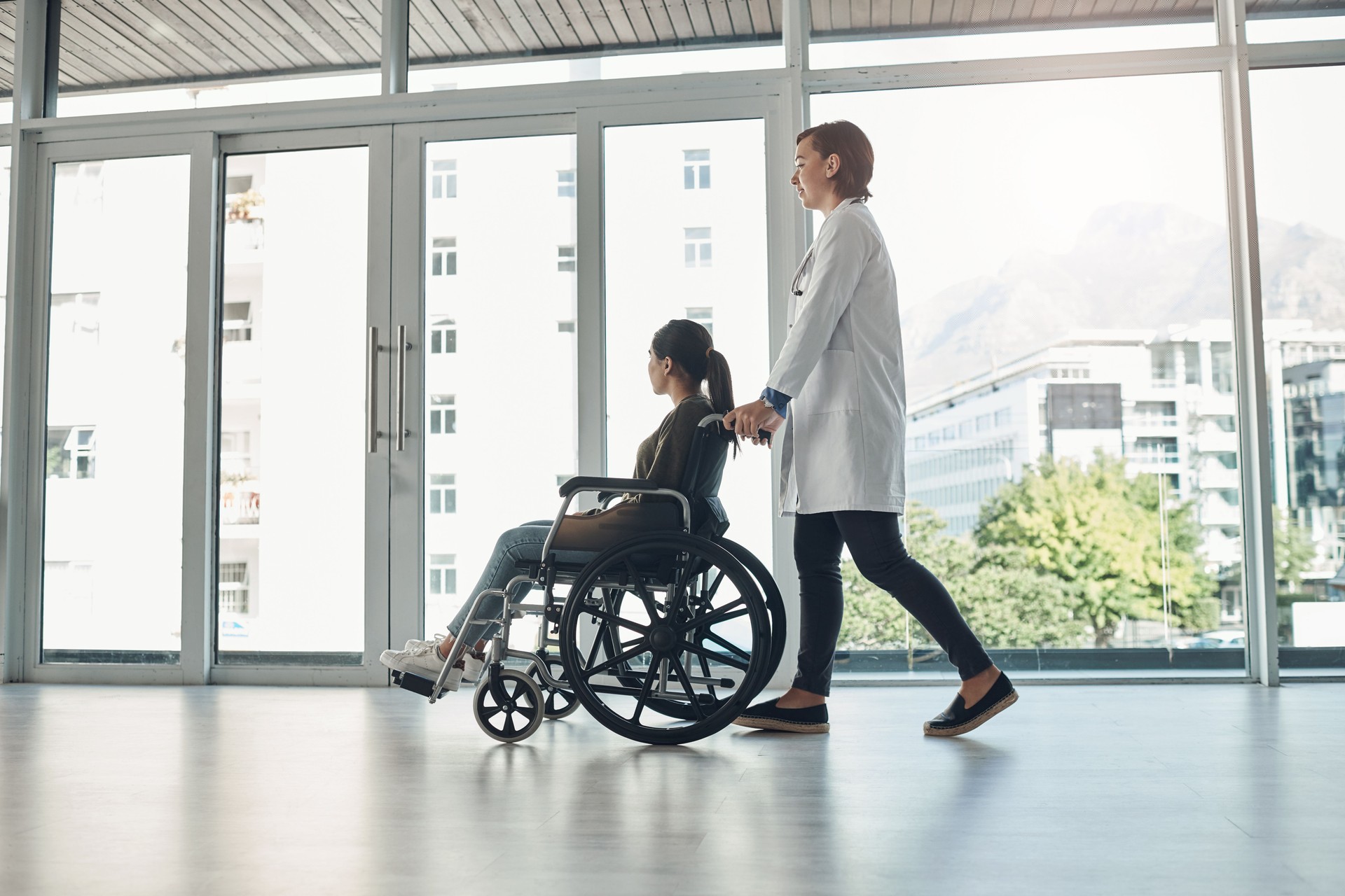 Shot of a young female doctor pushing a patient in a wheelchair in a hospital